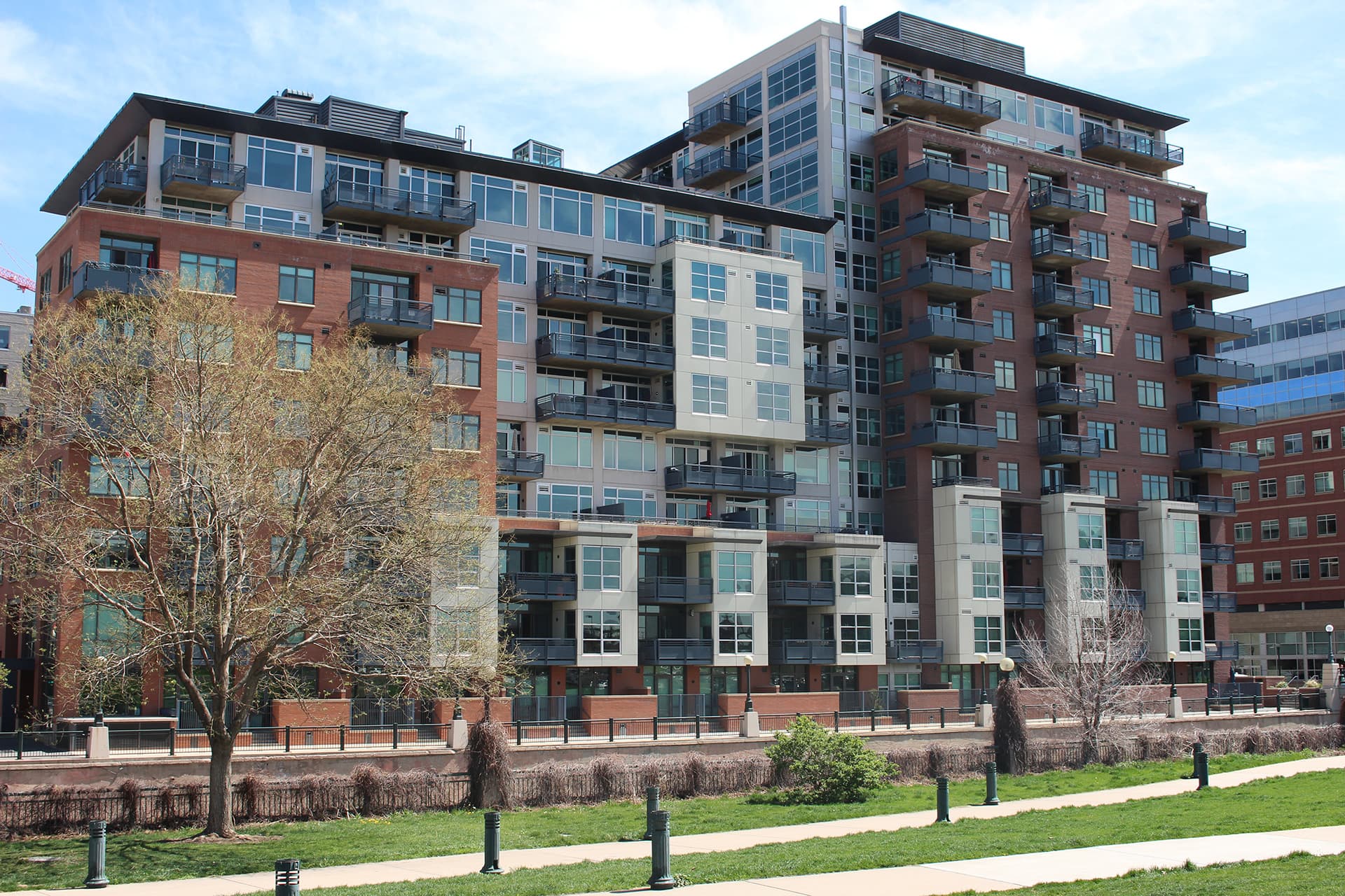 Waterside Lofts, a brick and grey apartment building beside a riverside path in Denver