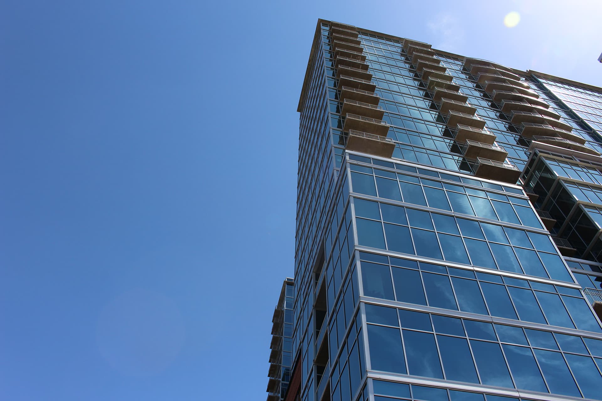 Glass residential high-rise with stacked balconies, seen from below